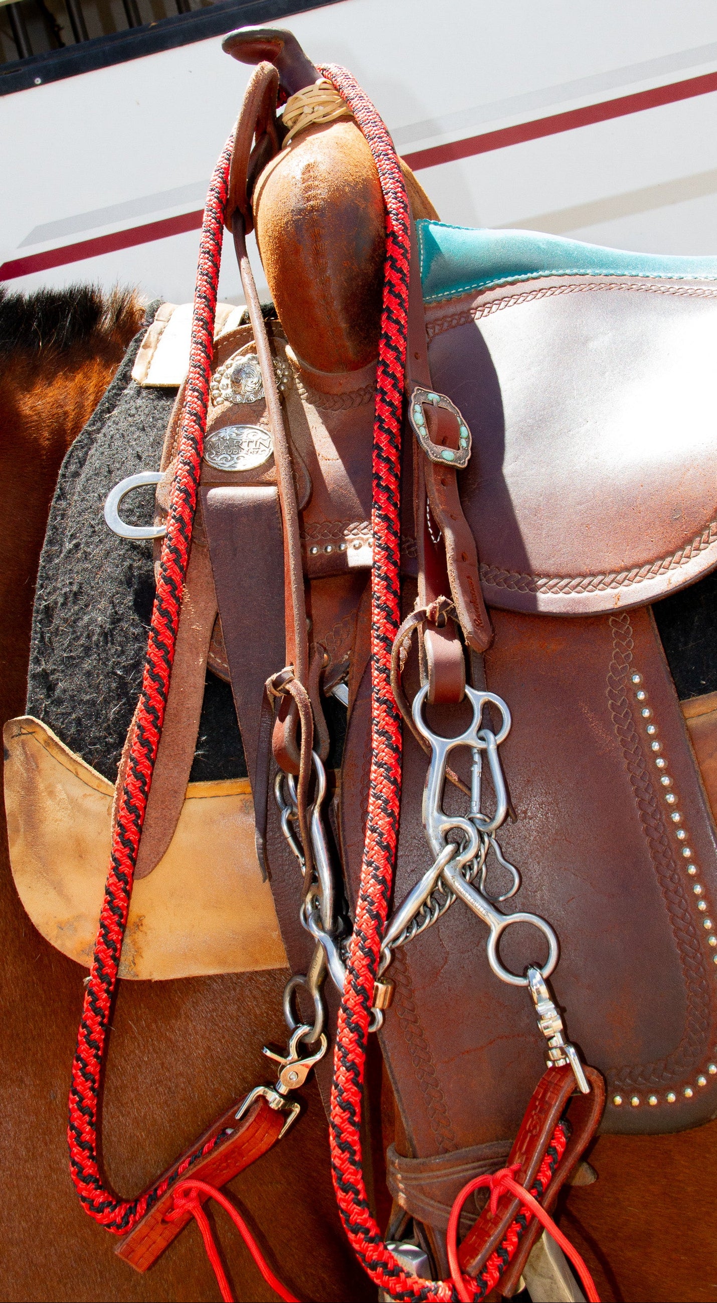 Close-up of a horse saddle with reins on a horse, with a vehicle in the background.