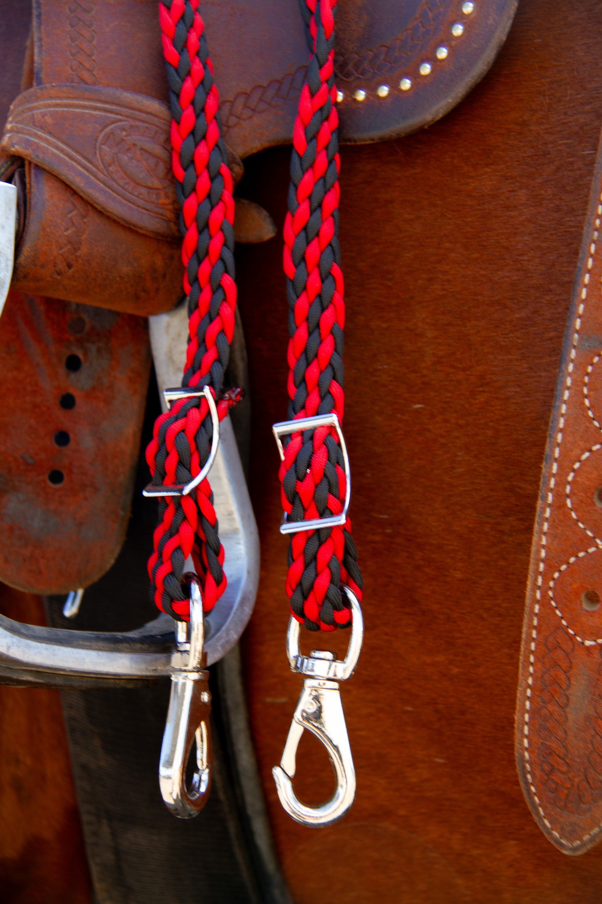Red and black braided reins with silver hardware on a brown leather saddle.