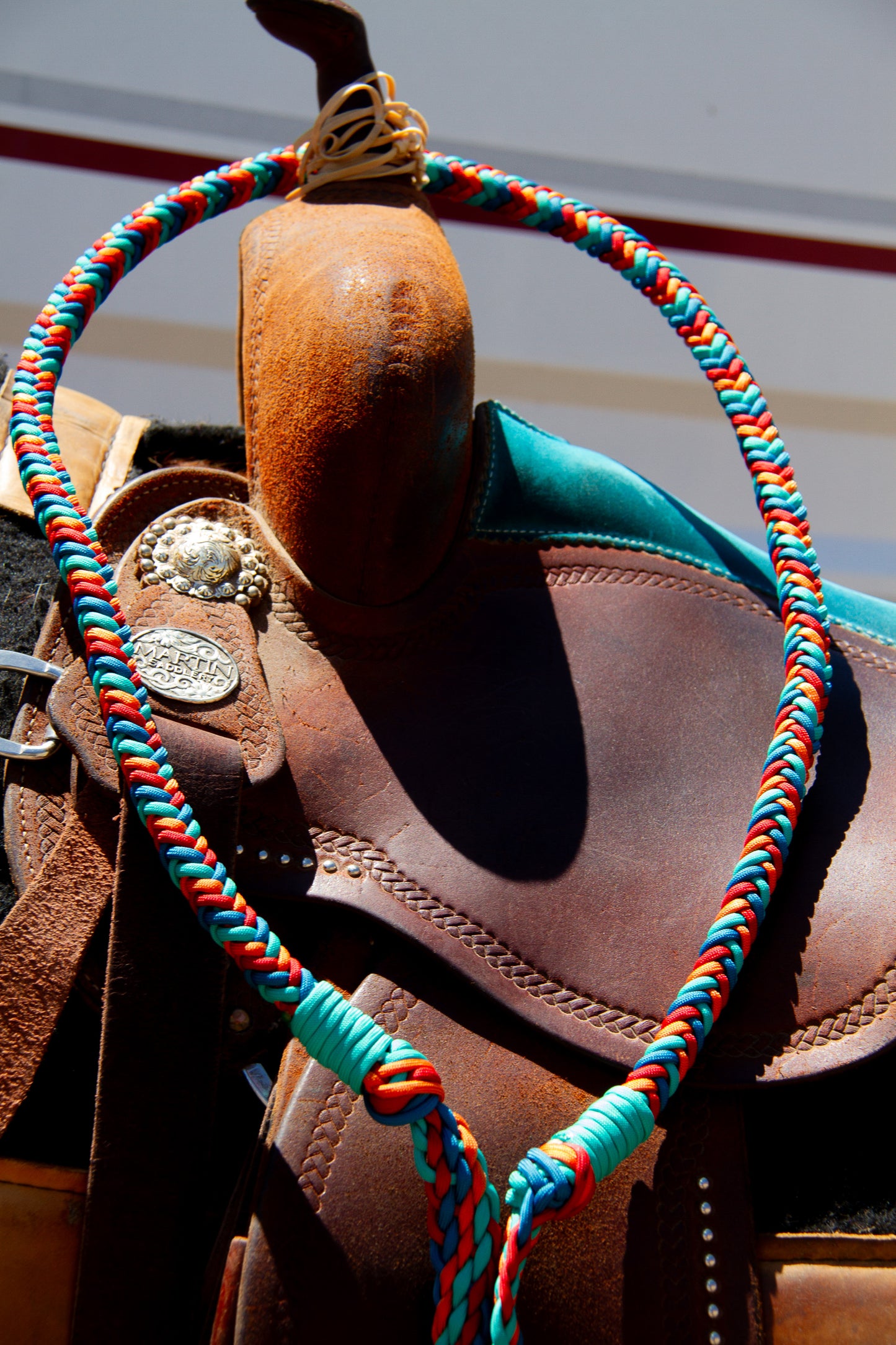 Brown leather saddle with colorful reins on a blurred background