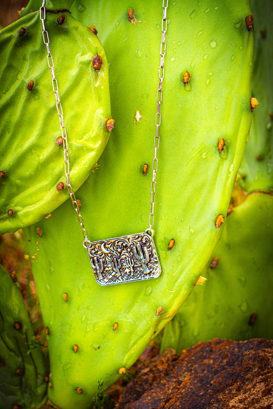 Silver necklace with a rectangular cactus landscape pendant on a green cactus surface
