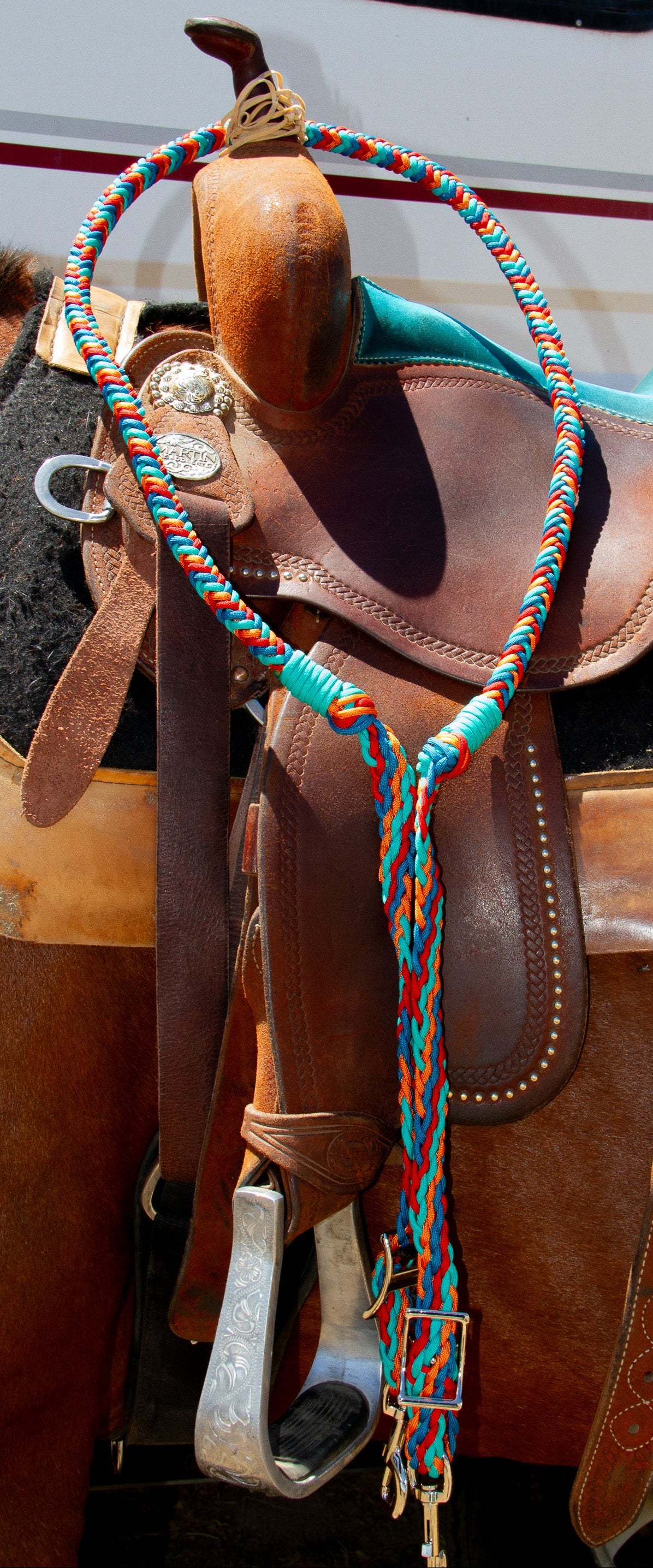 Brown leather saddle with colorful reins on a horse, with a vehicle in the background.